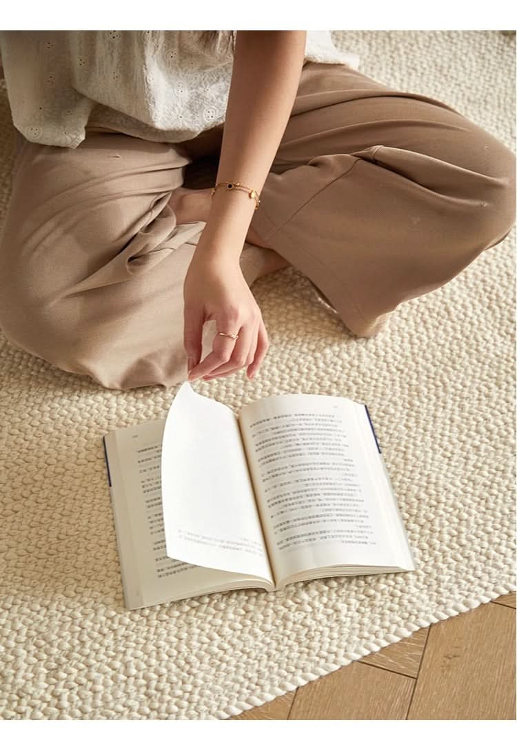 Natural cream braided wool rug with open book and person reading.